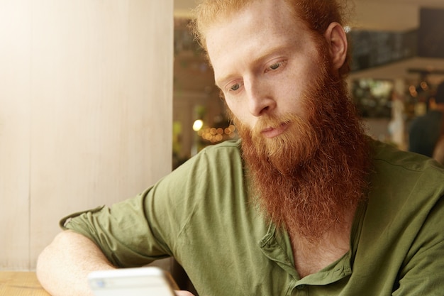 Jonge gember man met telefoon in café