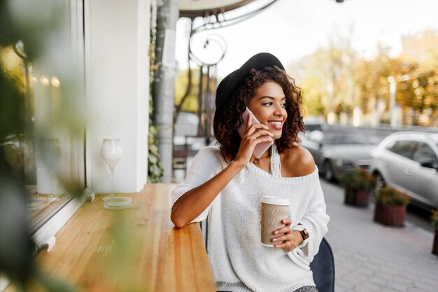 Jonge gemengde vrouw met afro kapsel praten via de mobiele telefoon en glimlachen