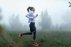Gratis foto jonge gemotiveerde sportvrouw die op mistige ochtend in het park loopt