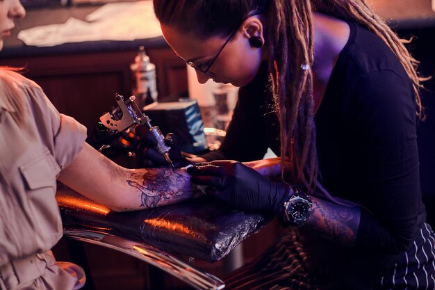 Jonge gerichte tattoo-meester maakt tatoeage op de hand van de klant in een donkere tattoo-salon.