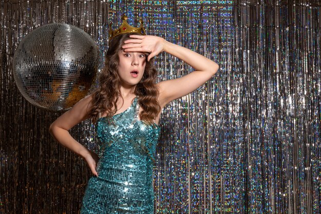 Jonge geschokt mooie dame draagt blauwgroene glanzende jurk met pailletten met kroon in het feest