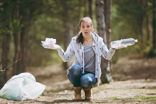 Jonge geschokte vrouw in vrijetijdskleding die handen schoonmaakt en verspreidt met afval in park op groene muur Premium Foto
