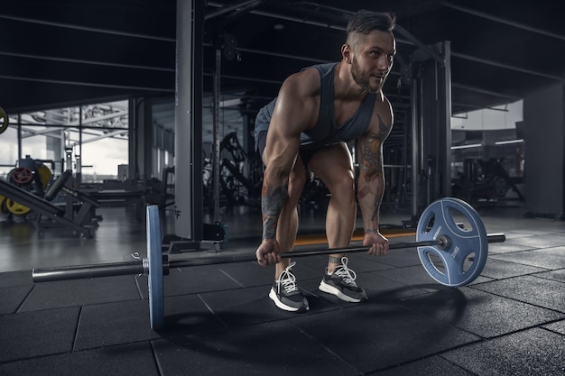 Jonge gespierde atleet oefenen pull-ups in de sportschool met barbell