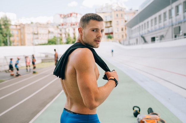 Jonge gespierde man terugkijkend over zijn schouder. portret van een knappe man blauwe korte broek.