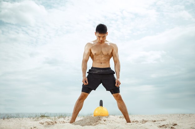 Jonge gezonde man atleet doen squats op het strand