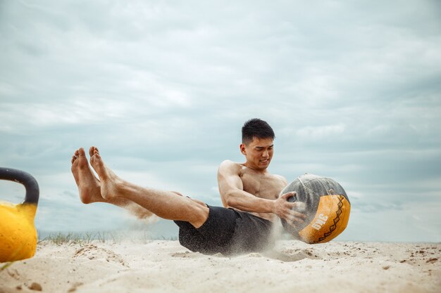 Jonge gezonde man atleet doet squats op het strand