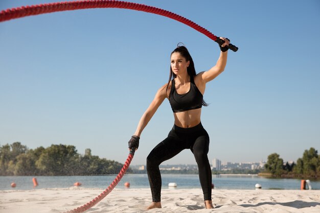 Jonge gezonde vrouw die oefening met de touwen doet op het strand