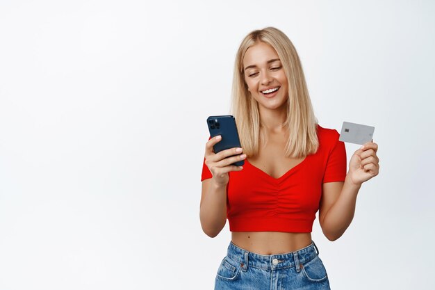 Jonge glimlachende vrouw die mobiele telefoon en creditcard gebruikt om online te bestellen en te betalen met smartphone witte achtergrond