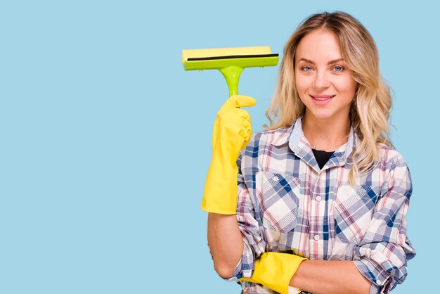 Jonge glimlachende vrouw die plastic wisser houden bekijkend camera tegen blauwe achtergrond