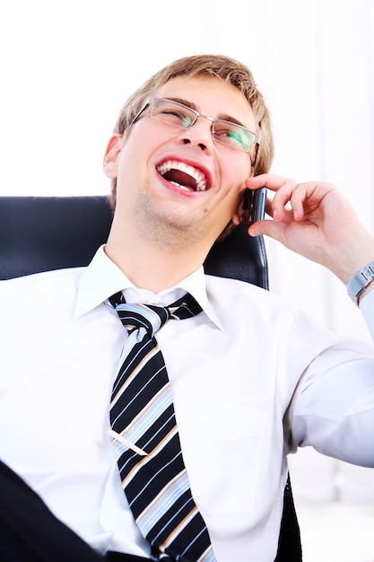 Jonge glimlachende zakenman die celtelefoon met behulp van