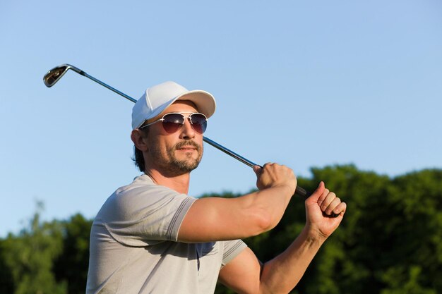 Jonge golfer die een schot slaat met een strijkijzer Volwassen man met een zonnebril die geniet van een professioneel spel op een groene baan