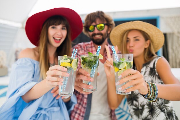 Jonge hipster gezelschap van vrienden op vakantie in zomerterras, mojito cocktails drinken, gelukkig positieve stijl, glimlachen gelukkig, twee vrouwen en man die samen plezier hebben, praten, flirten, romantiek, drie