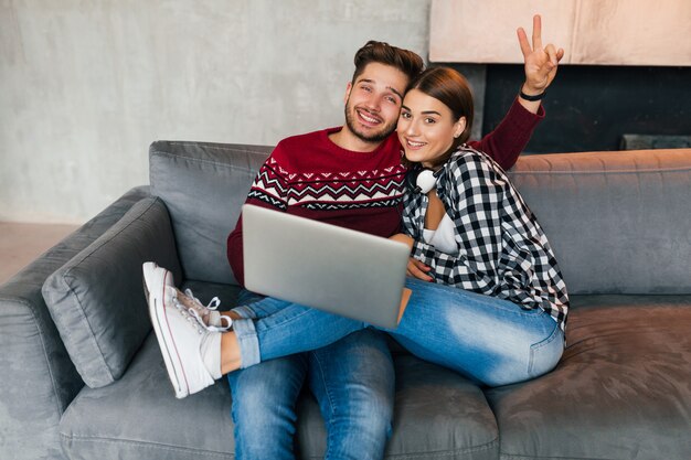Jonge hipster lachende man en vrouw om thuis te zitten in de winter, laptop bedrijf, koppel op vrije tijd samen, online studeren, freelancer, gelukkig, daten, duim opdagen, positief, in de camera kijken