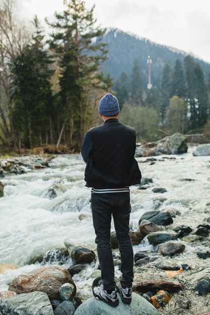 Jonge hipster man lopen op een rots aan de rivier in winter woud