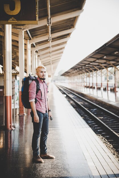 Jonge hipster man wachtend op het station platform met rugzak. Reisconcept.