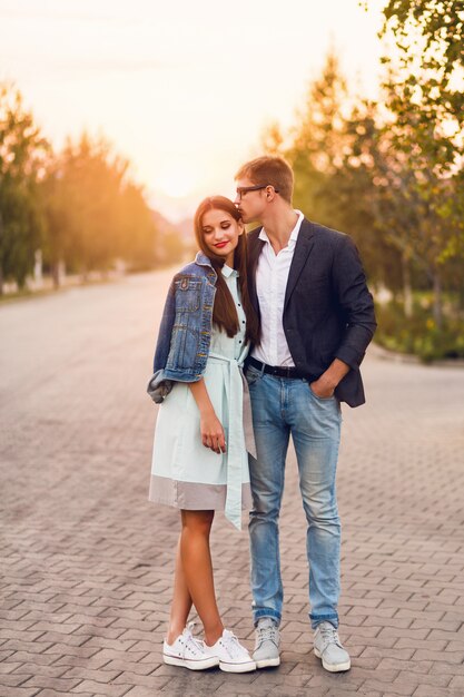 Jonge hipster paar verliefd buiten. Prachtig sensueel portret van jonge stijlvolle mode paar poseren in de zomer zonsondergang. Vrij jong meisje in jeansjasje en haar knappe vriend die lopen.