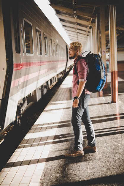 Jonge hipster toerist met rugzak op het treinstation. Vakantie toeristische concept.