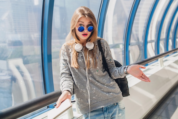 Jonge hipster vrouw in casual outfi in trui en zonnebril, student maken van aantekeningen, verbaasde gezichtsuitdrukking, probleem