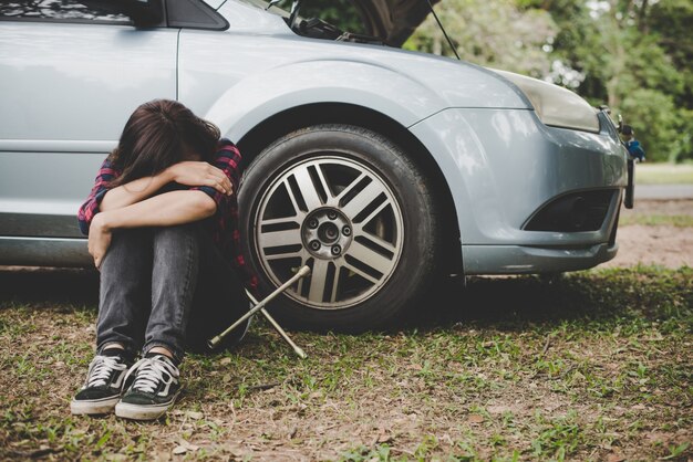 Jonge hipster vrouw wacht op wegenhulp nadat haar auto afgebroken is aan de kant van de weg die tegen haar auto zit.