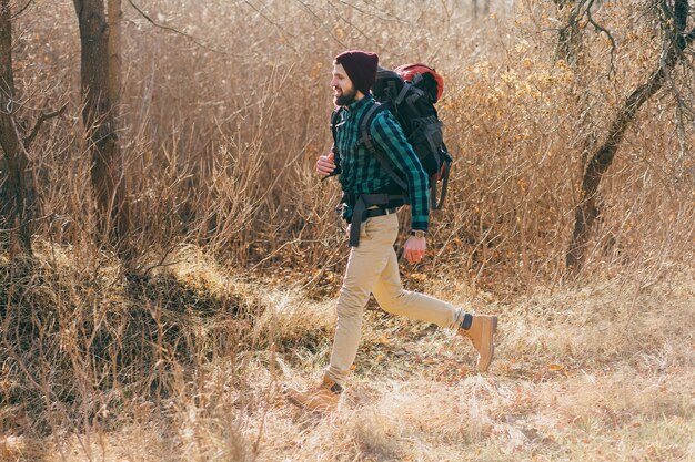 Jonge hipstermens die met rugzak in herfstbos reist die geruit overhemd en hoed draagt