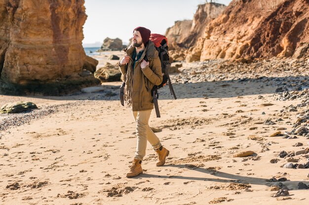 Jonge hipstermens die met rugzak reist in de herfstzeekust met een warme jas en muts?