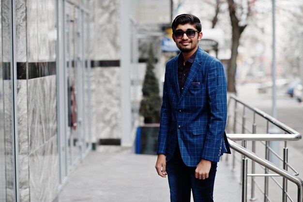 Jonge Indiase man op blauw pak en zonnebril poseerde buiten