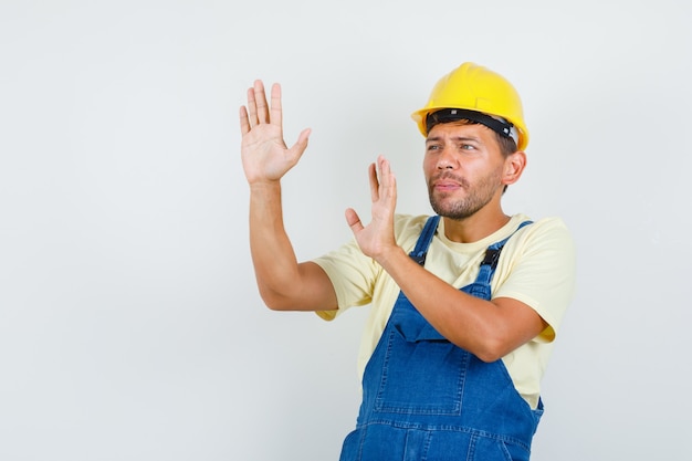 Jonge ingenieur die stopgebaar in uniform toont en bang kijkt. vooraanzicht.