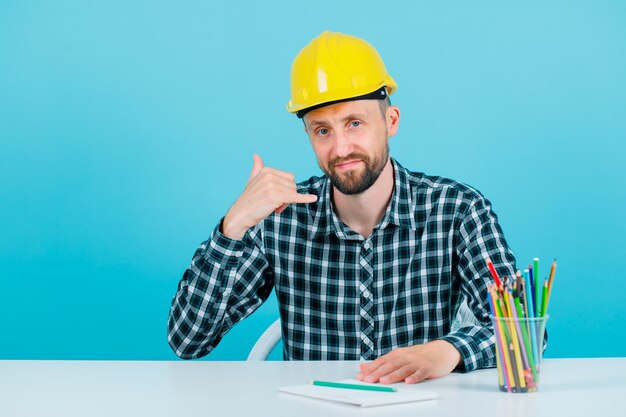 Jonge ingenieur man toont telefoongebaar door te kijken naar camera op blauwe achtergrond