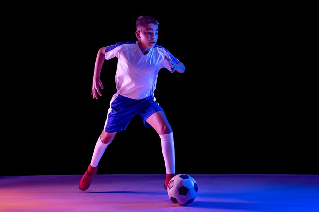Jonge jongen als voetbal of voetballer op donkere studio
