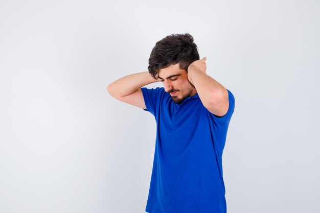 Jonge jongen die de handen op de oren drukt in een blauw t-shirt en er gehaast uitziet. vooraanzicht.