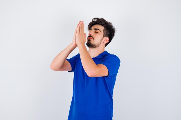 Jonge jongen die in gebed staat in een blauw t-shirt en er serieus uitziet. vooraanzicht.