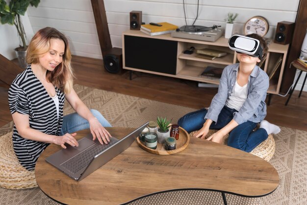 Jonge jongen die met virtuele werkelijkheid speelt terwijl de moeder werkt