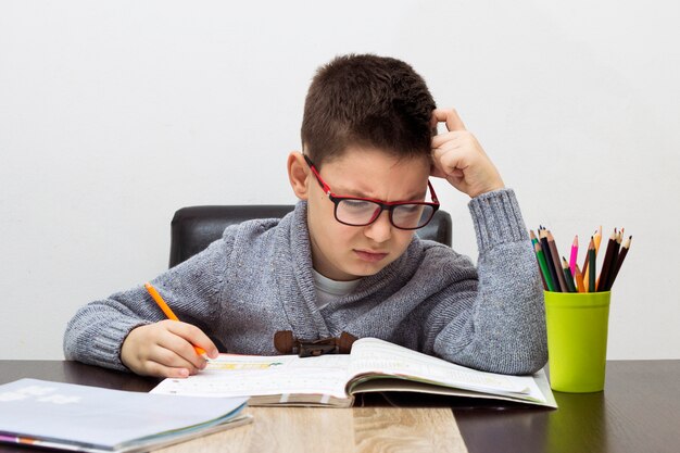 Jonge jongen gefrustreerd over huiswerk, thuis schrijven. Jongen studeert aan tafel. Kid tekening met een potlood.