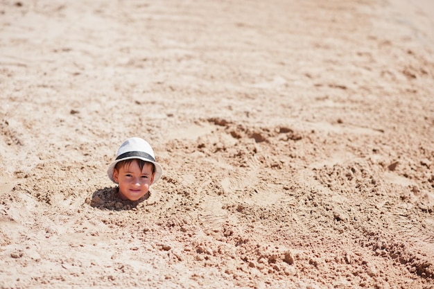 Gratis foto jonge jongen hoofd op zand draagt panama hoed grappige zomervakantie