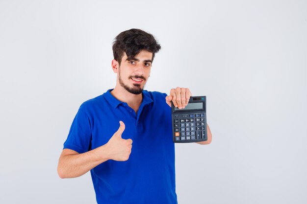 Gratis foto jonge jongen in blauw t-shirt met rekenmachine en duim opdagen en er gelukkig uitzien, vooraanzicht.