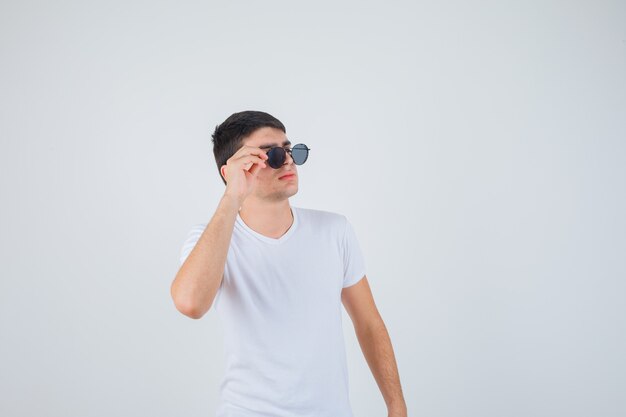 Jonge jongen met bril, opzij kijkend in t-shirt en op zoek naar cool, vooraanzicht.