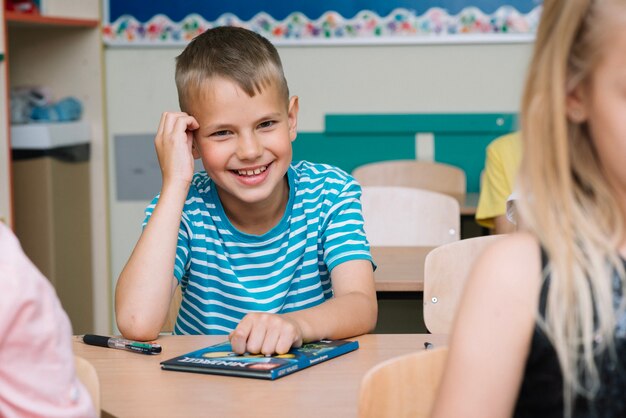 Jonge jongen zit in klaslokaal glimlachend