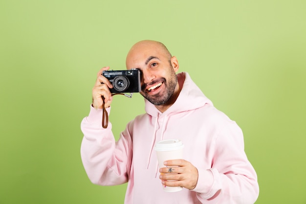 Gratis foto jonge kale blanke man in roze hoodie geïsoleerd, positieve greepcamera en kopje koffie