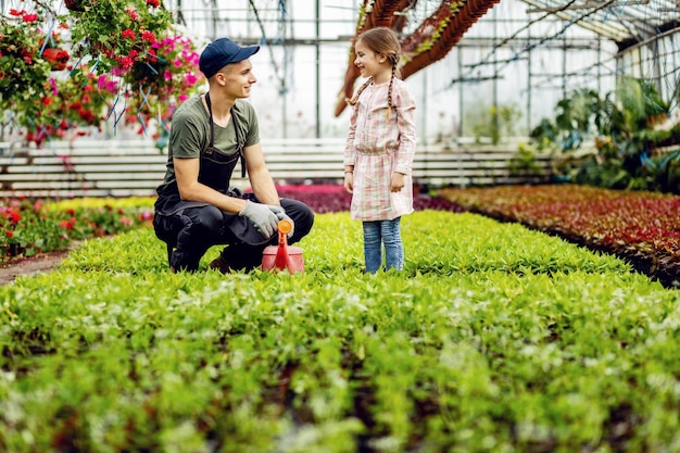 Jonge kasarbeider praat met een klein meisje terwijl hij planten voedt