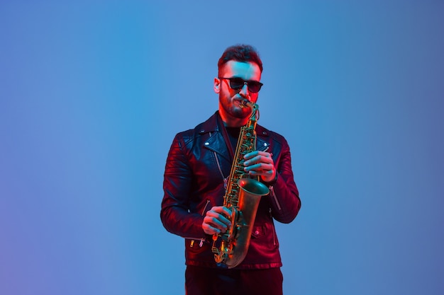 Jonge kaukasische jazzmusicus die de saxofoon speelt op gradiëntblauw-paarse studio in neonlicht