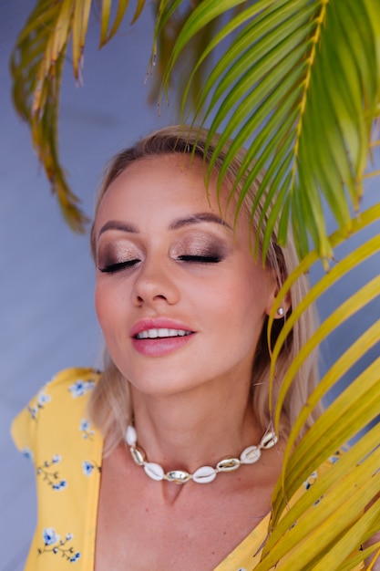 Jonge kaukasische kalme gelukkige mooie vrouw met heldere avondmake-up die de zomer gele kleding en zeeschelp halsketting draagt
