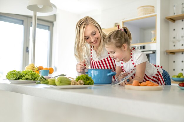 Jonge kaukasische moeder en dochter die bijpassende schorten dragen die soep samen in een keuken koken