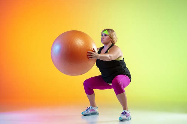 Jonge kaukasische plus size vrouwelijke model training op gradiënt oranje muur in neonlicht.