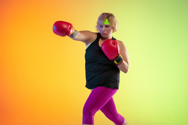 Jonge kaukasische plus size vrouwelijke model training op gradiënt oranje muur in neonlicht.