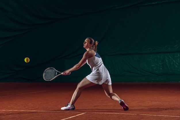 Jonge kaukasische professionele sportvrouw die tennis speelt op de muur van het sporthof.