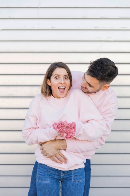 Jonge kerel die aantrekkelijke verbaasde dame met bloemen koestert