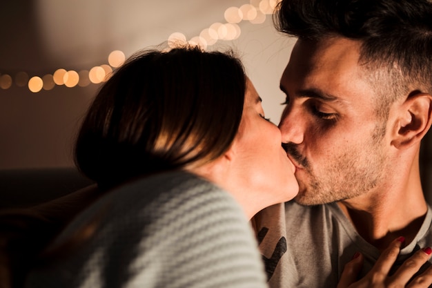 Jonge kerel kussen met dame in de buurt van fairy lights