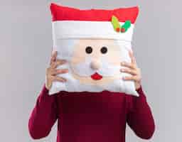 Gratis foto jonge kerel met kerstmuts met bril bedekt gezicht met kerst kussen geïsoleerd op een witte achtergrond