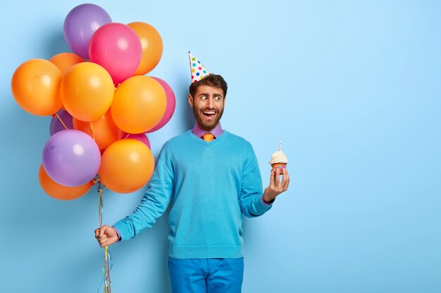 Jonge kerel met verjaardagshoed en ballonnen poseren in blauwe trui