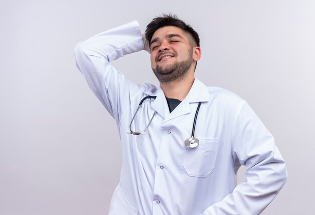 Jonge knappe arts die witte medische toga witte medische handschoenen en stethoscoop draagt